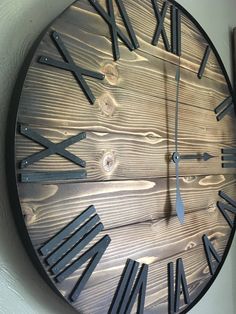 a wooden clock with roman numerals on the face and hands is hanging on a wall