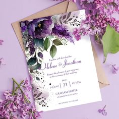 purple flowers and greenery are on top of the wedding card