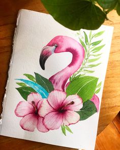 a pink flamingo sitting on top of a wooden table next to flowers and leaves