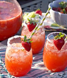 two glasses filled with strawberry mojitas and garnished with limes on a marble table