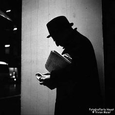 a man in a top hat and coat is reading a book while standing against a wall