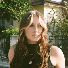 a woman with long hair standing in front of a house and looking at the camera