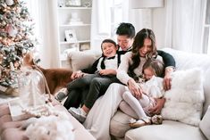 a family sitting on a couch in front of a christmas tree with their two children