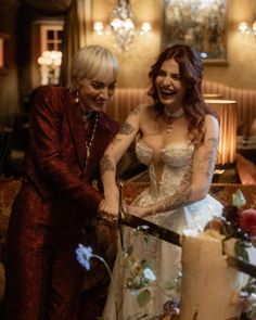 two women standing next to each other in front of a cake