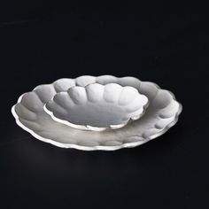 two white dishes sitting on top of a black tableclothed surface, one is shaped like a bowl and the other is shaped like a leaf