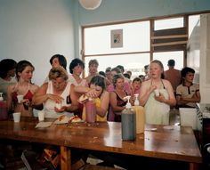 a group of people sitting at a table eating food and drinking sodas in front of them