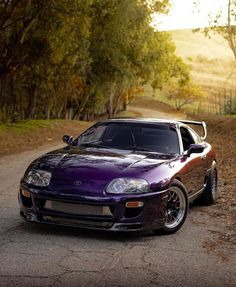 a purple sports car parked on the side of a road in front of some trees