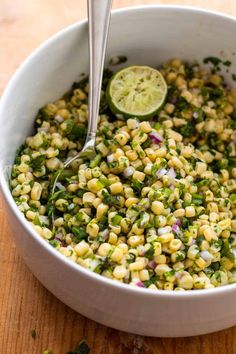 a white bowl filled with corn and garnished with cilantro, onions, and lime