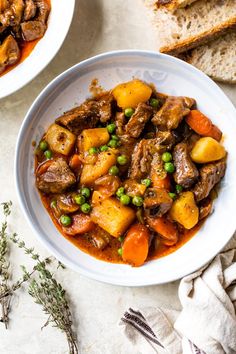 two bowls filled with stew next to slices of bread