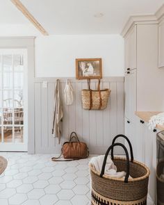 a laundry room with white walls and flooring has baskets hanging on the wall next to an ironing board