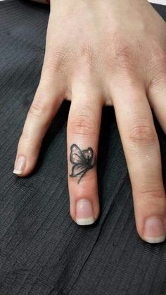 a woman's hand with a bow tattoo on her left thumb and ring finger