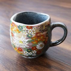 a coffee cup sitting on top of a wooden table with flowers painted on it's side