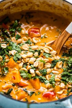 a wooden spoon in a pot filled with vegetables and beans, garnished with parsley