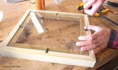 a person working on a wooden frame with some tools in front of him and another hand holding a pair of scissors