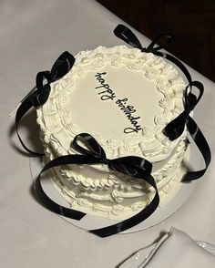 a white cake with black ribbon on top sitting on a table next to silverware