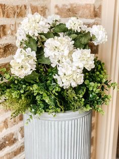 white flowers in a metal container on a brick wall