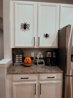 a kitchen decorated for halloween with white cabinets and black spider decorations on the upper cupboards