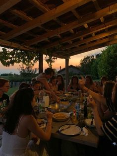 a group of people sitting around a table with food and drinks on it at sunset