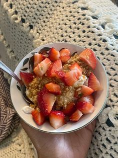 a person is holding a bowl of cereal with strawberries on top and oatmeal in the middle