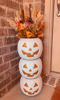 three pumpkins stacked on top of each other in front of a brick wall and door