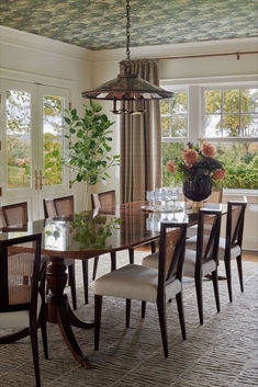 a dining room table with chairs and a potted plant in the center surrounded by windows