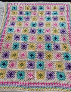 a crocheted blanket is laying on top of a white bed sheet with multicolored squares