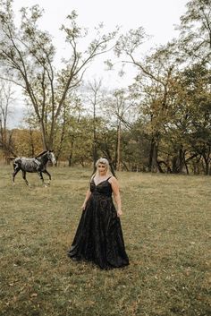 a woman in a black dress standing next to a horse