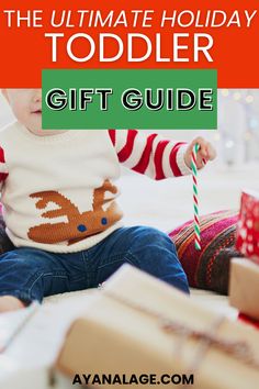 a toddler sitting on the floor with presents in front of her and text overlay that reads, the ultimate holiday toddler gift guide