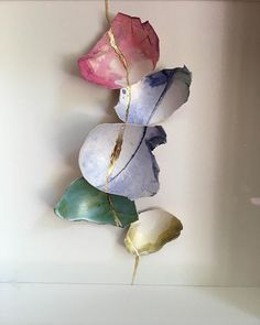 three different colored flowers are hanging from a string on a white wall in a room