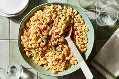 a bowl filled with pasta and vegetables on top of a tiled floor next to two glasses