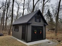 a small gray shed with wreaths on the door and windows is shown in front of some trees