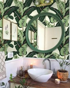 a bathroom with a mirror, sink and wallpaper that has green leaves on it