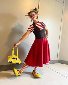 a woman dressed in clown makeup holding a yellow purse and wearing red striped tights