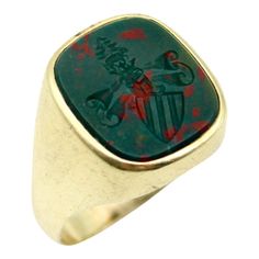 This is part of Chairish’s Fine Jewelry assortment.  This 14k gold Edwardian intaglio signet ring contains an esoteric image—a unique family crest with mysterious imagery. Carved into bloodstone, a striped shield sits on a diagonal, with a scroll looming above it. It is topped with a crown, a pine tree, and a tiny animal—perhaps a horse, coyote, or deer—who seems to shape shift each time it is looked at under the loop. The ambiguity of the image is sure to evoke thought. The bezel set bloodstone Red Blood, Pinky Ring, Size 10 Rings, Family Crest, Wax Seals, Green Stone, Pine Tree, Signet Ring, Deer