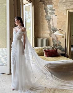 a woman in a white wedding dress is standing near a bed and looking off to the side