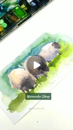 the watercolor sheep is sitting on the table next to the paintbrush and paper