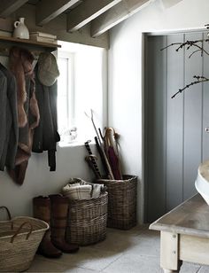 a room with several baskets and coats hanging on the wall next to a bench in front of a window