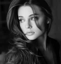 a beautiful woman with long hair posing for a black and white photo in the dark