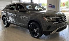 a grey volkswagen suv is parked in a showroom with tile flooring and large windows