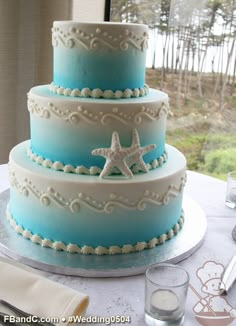 a three tiered blue and white wedding cake with starfish on the top layer