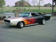 an old muscle car with flames painted on it's hood parked in front of a house