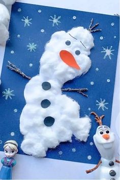 a snowman made out of cotton balls on top of a blue paper with two small figures next to it