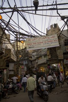 many people are walking through an alleyway with electric wires overhead and signs above them