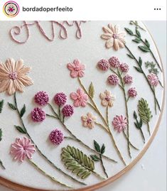 a close up of a embroidery pattern on a hoop with pink flowers and green leaves