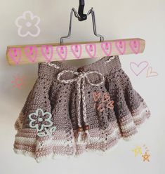 a crocheted skirt hanging on a wooden hanger with hearts and flowers drawn on it