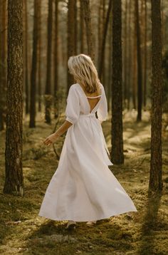 a woman in a white dress walking through the woods with her back to the camera