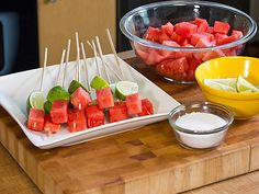 watermelon and lime skewers are on a cutting board next to a bowl of yogurt