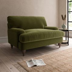 a green couch sitting on top of a hard wood floor next to a glass vase