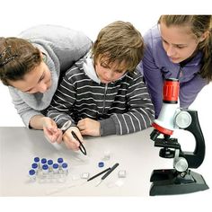 two girls and a boy looking at something on a table with a microscope in front of them