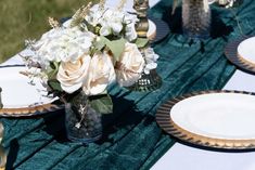 the table is set with white and gold plates, silverware, and flowers in a vase